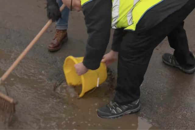Mark Morrell buckets out water to show Matt Allbright, sweeping, the depth of the pothole