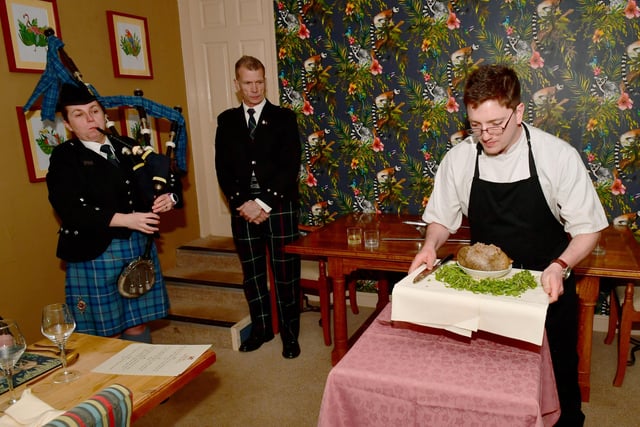 Addressing the Haggis is John Mackenzie.  Kirsteen Macdonald of RAF Waddington pipes and drums, and apprentice chef Blue Charles carrying the haggis. EMN-220126-102443001