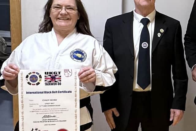 Senior Master Cindy Moss proudly displays her International Black Belt Certificate following her promotion, pictured alongside Grand Master Cargin Moss MBE, whose guidance and leadership marked a significant moment in the ceremony