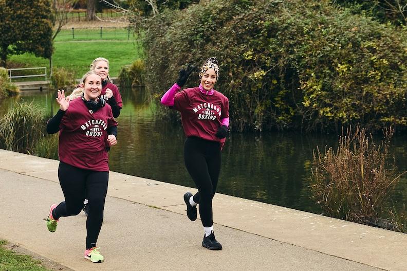 Runners give a wave to the photographer as they head around the lake at Abington Park