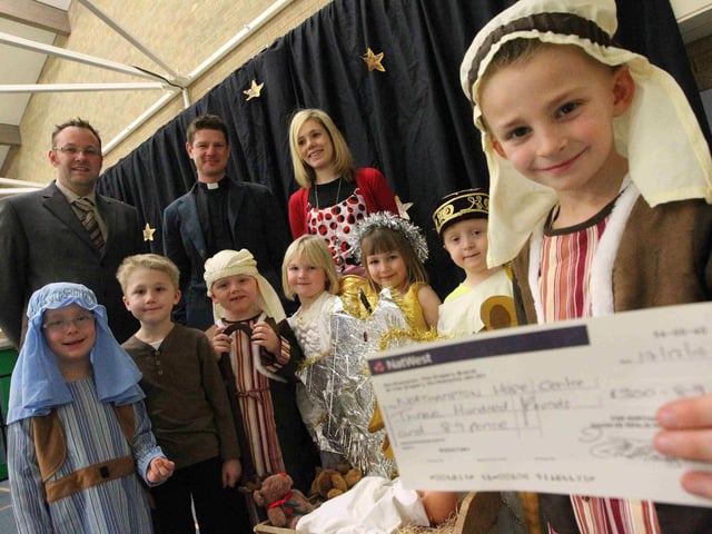 Simon Senlis Primary School -  cheque presentation to the Hope Centre with children from the Reception nativity and from St Benedicts Church. Adults left to right are Head Elliot Howles, Rev Marcus Purnell and Helen Harris from Hope Centre