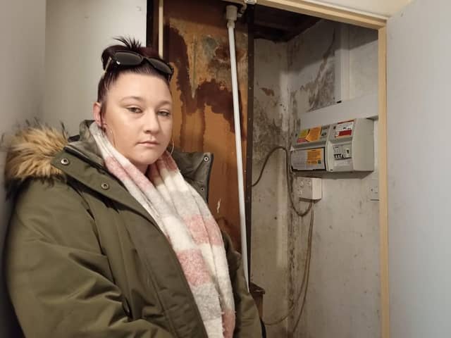 Chelsea Day stood next to the electricity box cupboard in her NPH flat which has a water leak coming from the ceiling and black mould sprouting on the walls