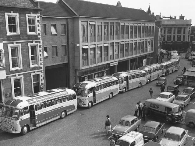 At least eight Wesleys coaches gather on Northampton Market Square to take passengers on an outing. Outside the Peacock Way arcade. September 10, 1964