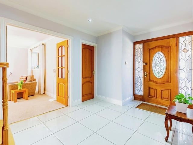 The spacious hallway is light and airy, with white tiled flooring and an oak wood finish