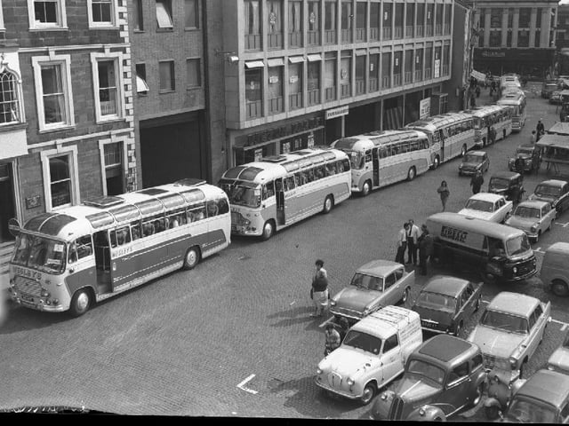 At least eight Wesleys coaches gather on Northampton Market Square to take passengers on an outing. Outside the Peacock Way arcade. September 10, 1964