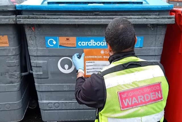 A Neighbourhood Warden applying a sticker to a commercial bin