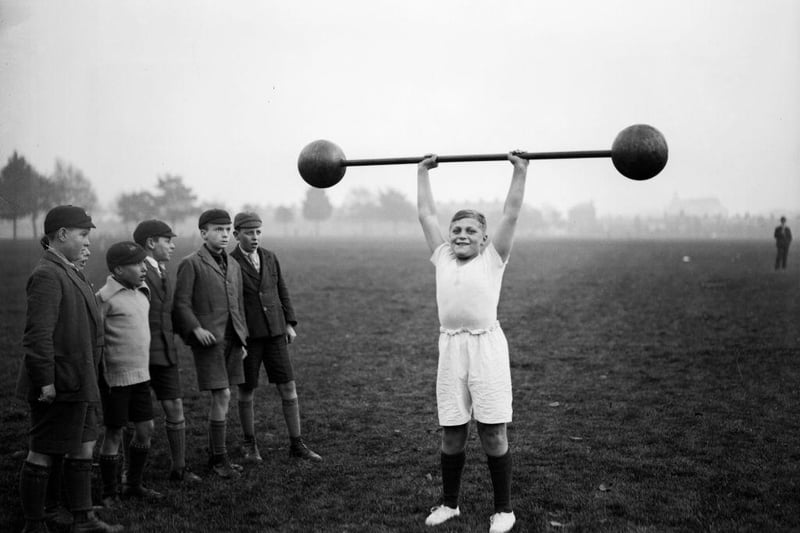 Northampton schoolboy William Albert Tuckley raises a dumb-bell weighing 110 pounds above his head, to the amazement of his classmates. Eleven-year-old Tuckley is being trained by Mr French, weightlifting champion of Northamptonshire and Buckinghamshire.  The pic was taken on 22nd October 1931.