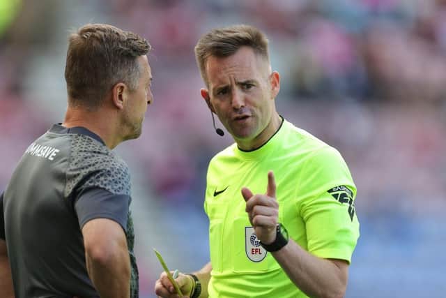 Referee Ross Joyce talks to Cobblers boss Jon Brady prior to showing him a yellow card during the Sky Bet League One match between Wigan Athletic and Northampton Town at DW Stadium on August 12, 2023 in Wigan, England. (Photo by Pete Norton/Getty Images)