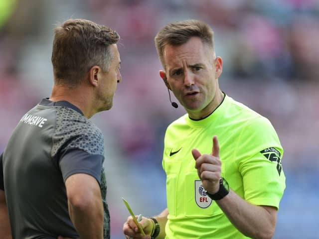 Referee Ross Joyce talks to Cobblers boss Jon Brady prior to showing him a yellow card during the Sky Bet League One match between Wigan Athletic and Northampton Town at DW Stadium on August 12, 2023 in Wigan, England. (Photo by Pete Norton/Getty Images)