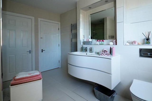 A second glimpse of the family bathroom, which boasts underfloor heating. Note the attractive top-mounted sink with vanity unit and fixed mirror. There are two chrome heated towel-rails, a feature radiator, fully tiled walls, a tiled floor, a dual shaver point and a built-in store or linen cupboard.