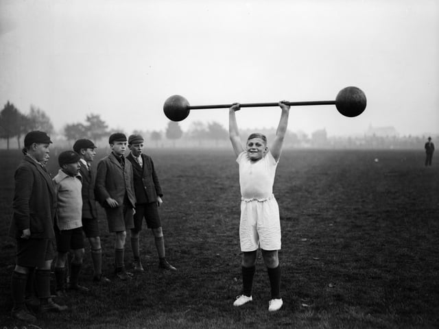 22nd October 1931: Northampton schoolboy William Albert Tuckley raises a dumb-bell weighing 110 pounds above his head, to the amazement of his classmates. Eleven-year-old Tuckley is being trained by Mr French, weightlifting champion of Northamptonshire and Buckinghamshire. (Photo by Fox Photos/Getty Images)