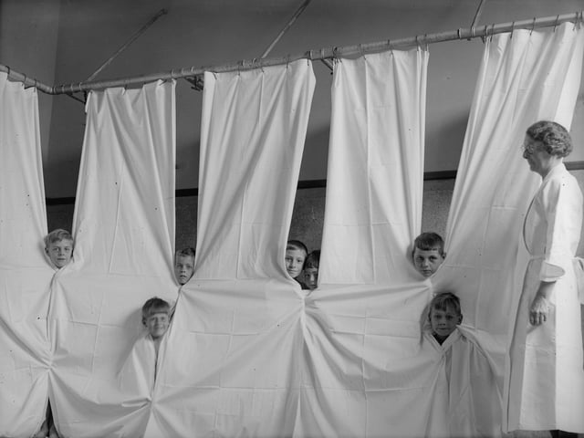 September 1934: Young boys peering through cubicle curtains at the Open Air Recovery School in Kettering, Northants. (Photo by Fox Photos/Getty Images)