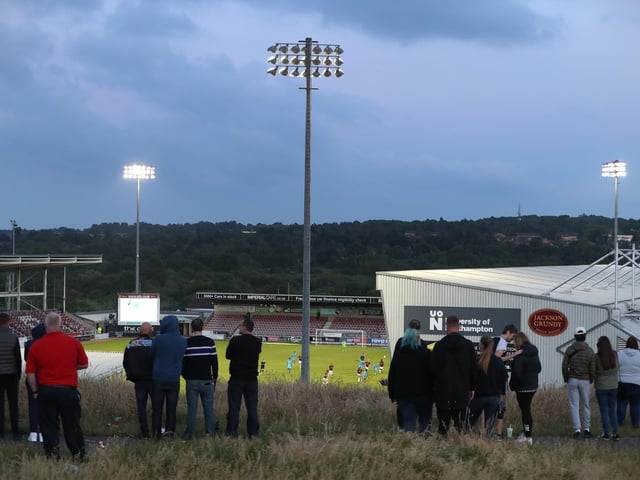 2020: Fans watch from a bank which overlooks the stadium during the Sky Bet League Two Play Off Semi-final 1st Leg match between Northampton Town and Cheltenham Town at PTS Academy Stadium on June 18, 2020 in Northampton, England. (Photo by David Rogers/Getty Images)