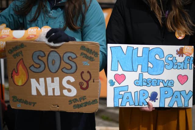 People hold placards calling for fairer pay on a picket line (Photo by Daniel LEAL / AFP) (Photo by DANIEL LEAL/AFP via Getty Images)