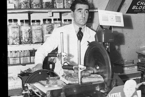 A blast from the past - this shopkeeper standing beside a bacon slicer, with jars of sweets on sale behind him