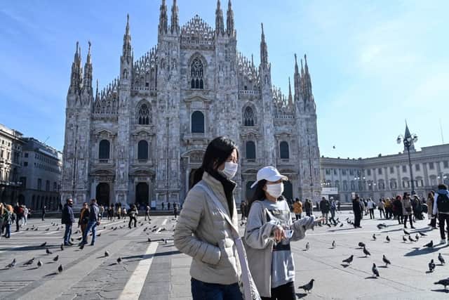 Two women wearing a protective facemask walk across the Piazza del Duomo, in front of the Duomo, in central Milan, on February 24, 2020