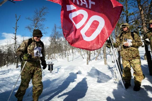 The RAF100 flag is waved at the finish line of the cross-country skiing race held on the final day of Exercise Wintermarch as one of the skiers crosses the line.
