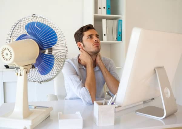 Casual businessman sitting at desk with electric fan in his office
