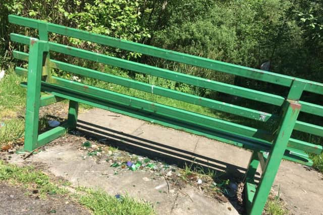 Smashed glass sits under a public bench overlooking the lake.