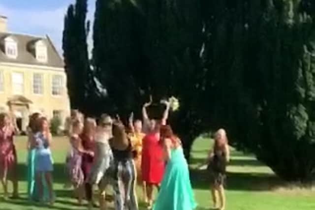 The bride flings the flowers into the crowd towards a group of women who all have their eyes on the prize.