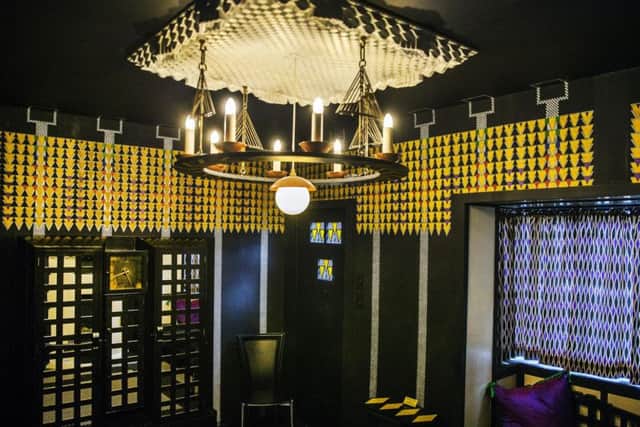 The theatrical lounge/hall was the point of entry into the house from the street. The room is most famous for its medievalist candelabrum, yellow and black geometric graphics and panels of decorative leaded glass to brighten the stairway from the kitchen downstairs,