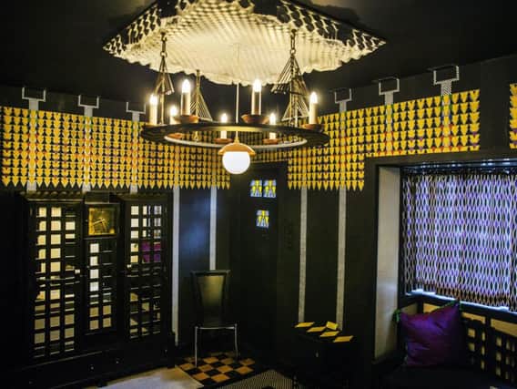 The theatrical lounge/hall was the point of entry into the house from the street. The room is most famous for its medievalist candelabrum, yellow and black geometric graphics and panels of decorative leaded glass to brighten the stairway from the kitchen downstairs,