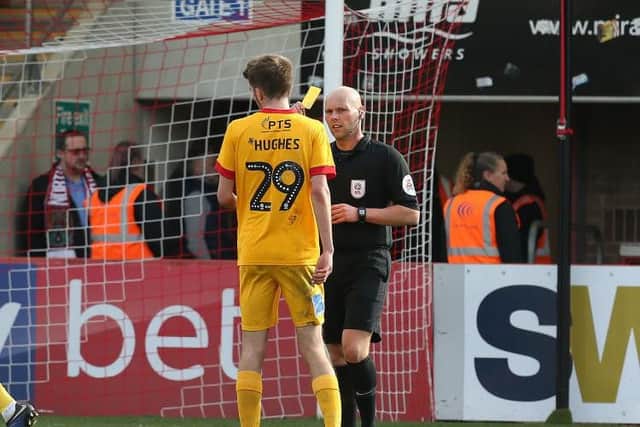 Teenager Ryan Hughes is shown yellow by referee Charles Breakspear after giving away a first-half penalty on his Cobblers debut at Whaddon Road. Pictures: Pete Norton