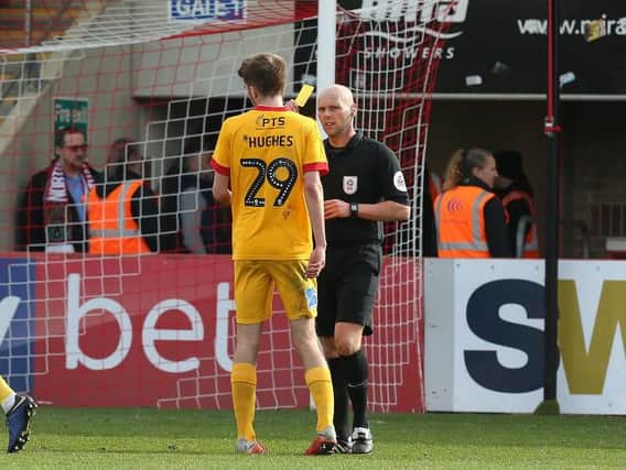 Teenager Ryan Hughes is shown yellow by referee Charles Breakspear after giving away a first-half penalty on his Cobblers debut at Whaddon Road. Pictures: Pete Norton