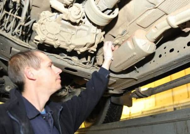 A mechanic points out the catalytic converter on the underside of a car